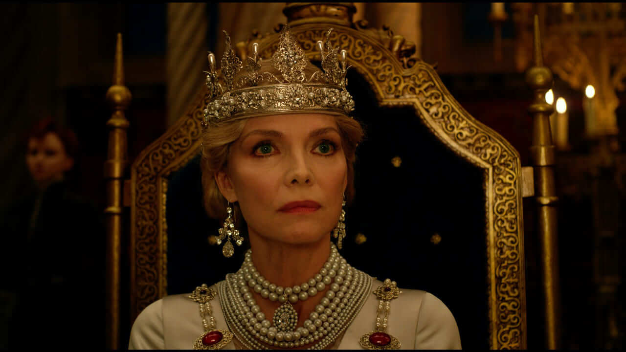 Queen Ingrith, in a jeweled crown and pearls, sits on a gold throne and stares coldly ahead