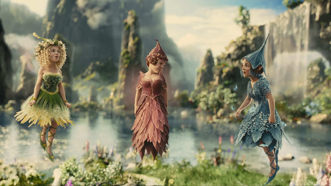The Moors in sunlight: three pixies in leaf and petal dresses hover over a pool among flowers, with waterfalls and tall green rock spires behind them