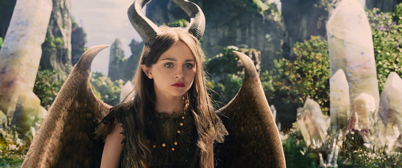 Young Maleficent, a girl with curling horns and brown feathered wings, stands among white crystals and green rock spires in the Moors