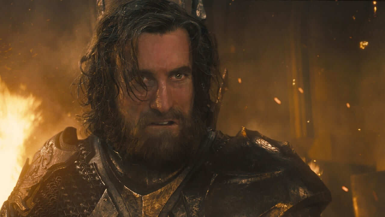 King Stefan, bearded and wild-eyed, in dark iron armor among flames and flying embers